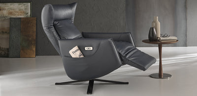 Black leather Batticuore Natuzzi Italia armchair, reclining, in a home setting next to a wooden side table with newspaper on.
