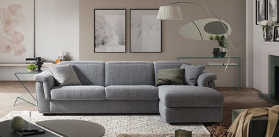 Grey fabric Curioso Natuzzi, corner sofa in a living room setting, with wooden floors and a white rug.