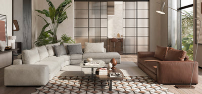 Living room setting with a Dominio Natuzzi grey fabric corner sofa and brown leather sofa with large house plants, wooden floors, a large rug and coffee table.
